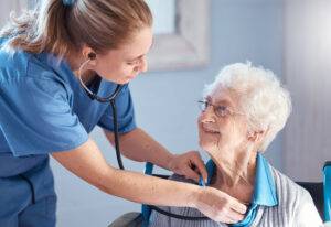 Seniorin und Krankenschwester, die Stethoskop zur Überprüfung von Herzschlag, Atmung und Gesundheit während der Beratung in der häuslichen Pflege benutzt.