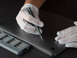 Mann repariert einen Apple Laptop in weißen Handschuhen mit einem Schraubenzieher und einem Satz Bits