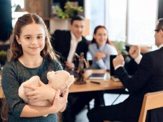 Glückliches kleines Mädchen umarmt Teddybär im Büro eines Familienanwalts.