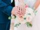 Hände von Braut und Bräutigam mit Eheringen auf schönem Rosenstrauß