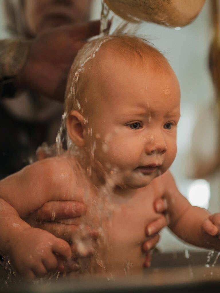 Ein Baby erlebt eine freie Taufe in Augsburg, umgeben von den fürsorglichen Händen seiner Familie, während es sanft mit Wasser übergossen wird