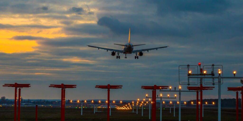 in Flugzeug nähert sich der Landebahn des Flughafens Nürnberg bei Dämmerung, beleuchtet von den Landelichtern, während der Himmel in warmen Farben schimmert