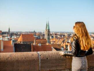 Eine Frau blickt über die Dächer von Nürnberg bei Sonnenuntergang, während sie eine Mauer an einem Aussichtspunkt hält – idealer Ausgangspunkt für Flüge vom Flughafen Nürnberg