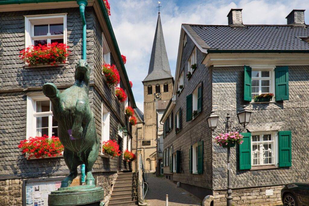 Die historische Altstadt von Mettmann mit Schieferhäusern, Blumen geschmückten Fenstern und einer Kirchturmspitze im Hintergrund – ideal für einen Ausflug nach der Registrierung von Autoschildern in Mettmann.