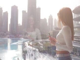 Frau blickt aus Fenster auf Dubai mit Wasser und Skyline