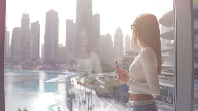 Panoramablick auf Dubais Innenstadt mit Wasserlandschaft Frau blickt aus Fenster auf Dubai mit Wasser und Skyline