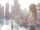 Frau blickt aus Fenster auf Dubai mit Wasser und Skyline