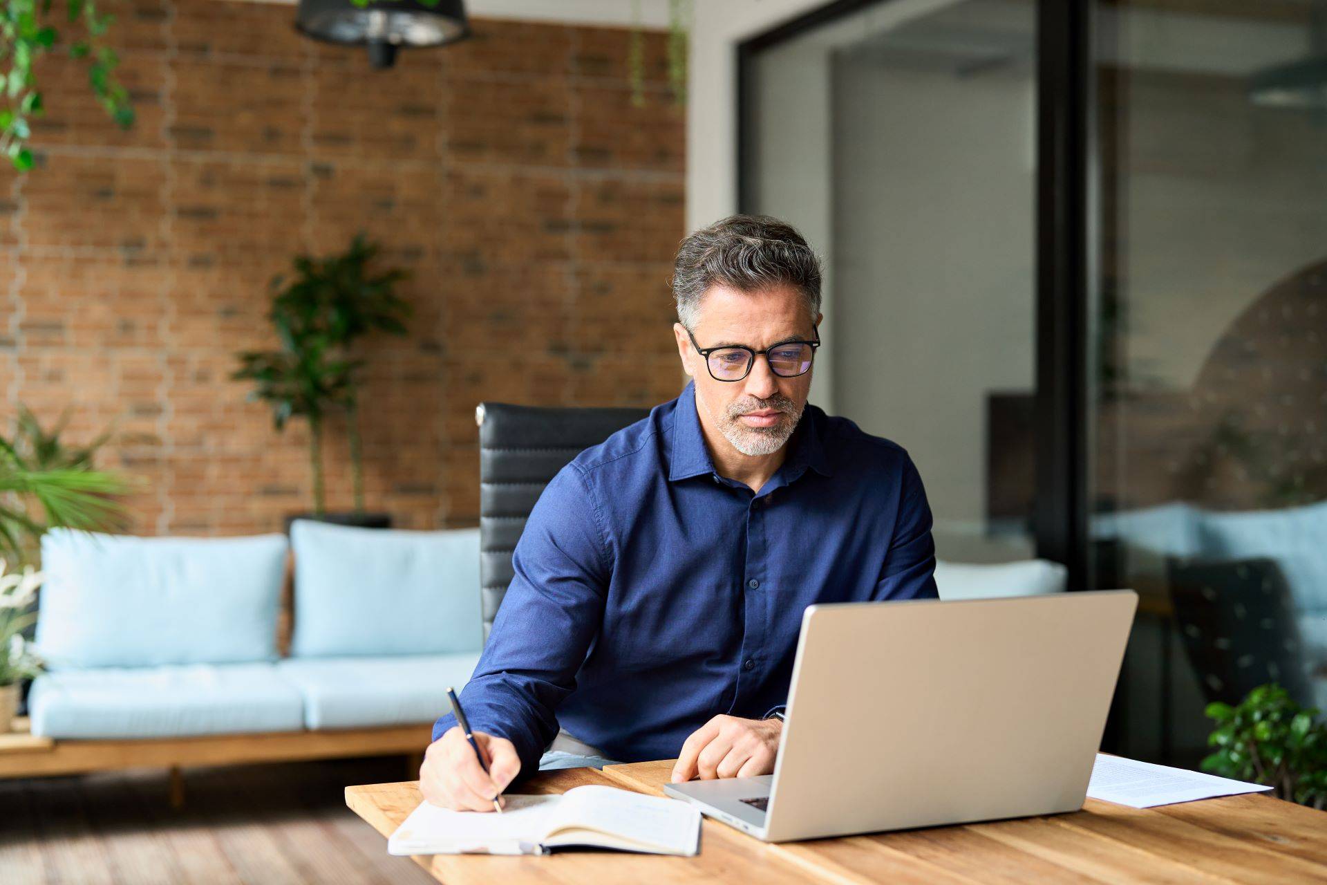 Mann arbeitet konzentriert am Laptop mit Notizen
