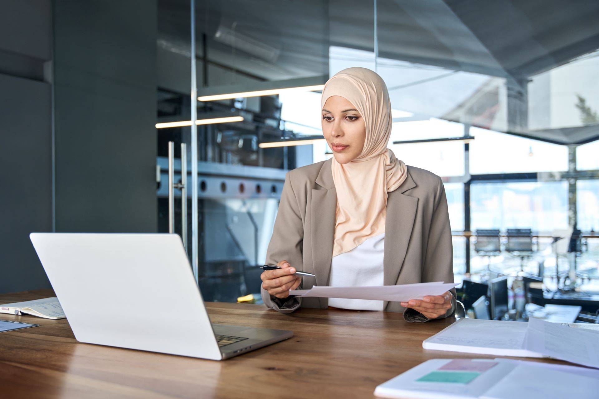 Frau prüft Dokumente vor Laptop in modernem Büro