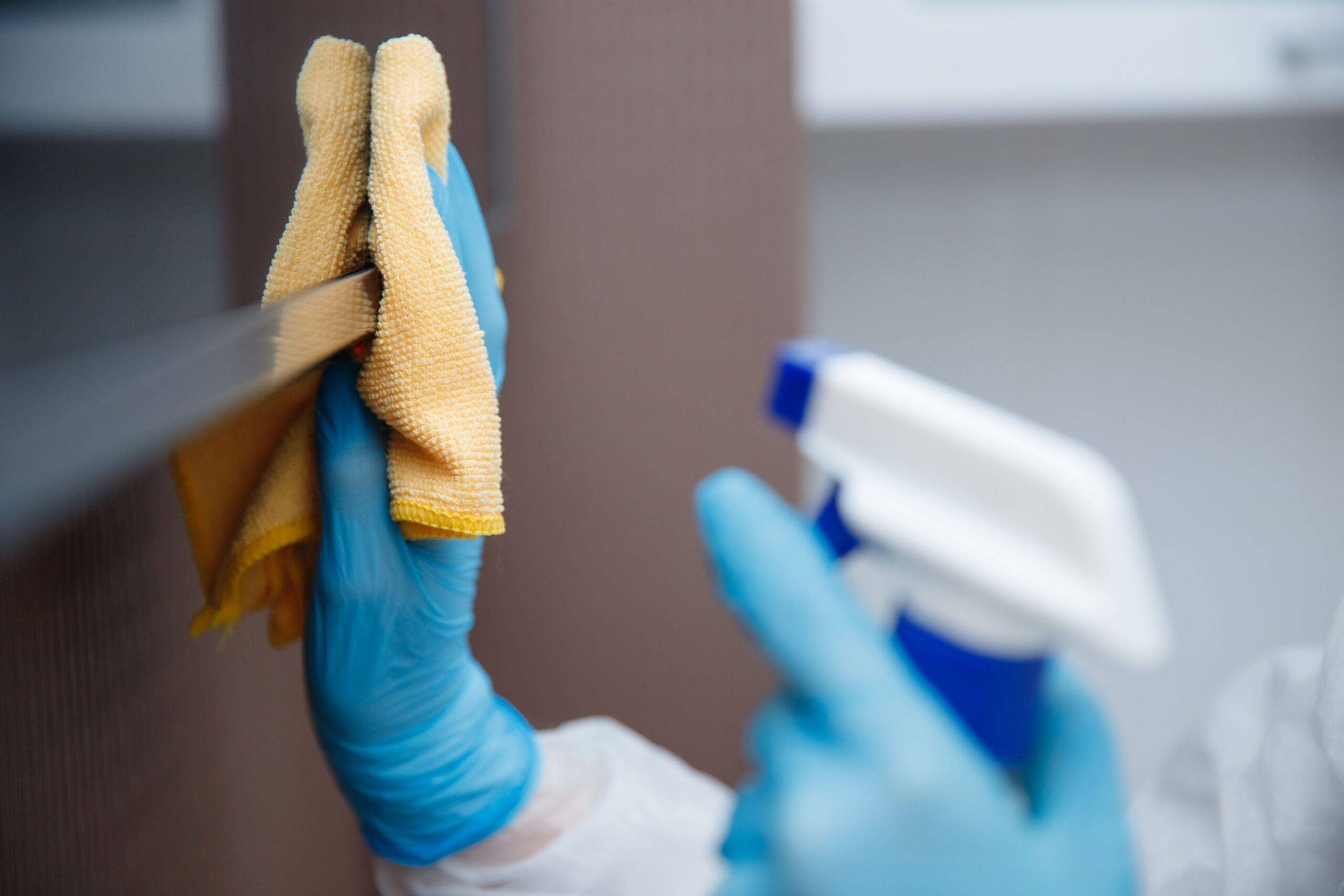Fachgerechte Reinigung einer Bürofläche mit Handschuhen und Desinfektionsspray
